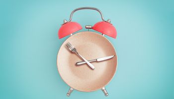 Reloj despertador y plato con cubiertos . concepto de ayuno intermitente, almuerzo, dieta y pérdida de peso