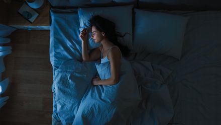 Vista de cima de uma bela jovem que dorme confortavelmente numa cama no seu quarto à noite. Cores nocturnas azuis com luz fraca e fria do poste de luz a brilhar pela janela.