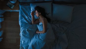 Vista dall'alto di una bella giovane donna che dorme comodamente su un letto nella sua camera da letto di notte. Colori notturni blu con una debole luce fredda di un lampione che brilla attraverso la finestra.