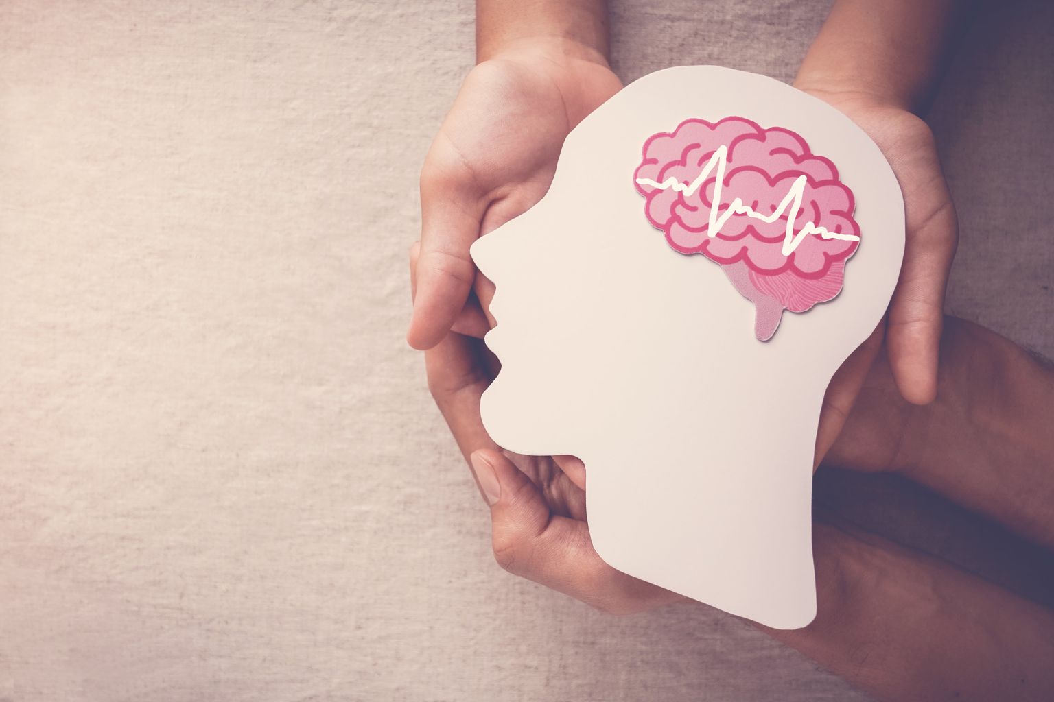 Dos pares de manos que sostienen una cabeza recortada en papel con un cerebro dibujado con una encefalografía simbólica que simboliza la epilepsia.