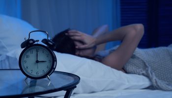 Donna infelice con insonnia sdraiata sul letto accanto alla sveglia di notte