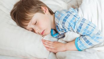 Um menino deitado na cama com os olhos fechados.