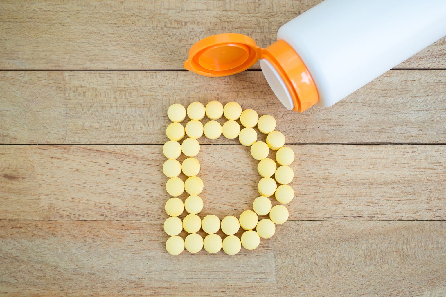 Yellow tablets are placed together to form the shape of the letter D on a wooden background.