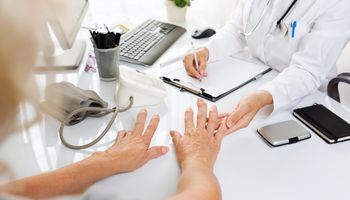 Close-up van een medisch onderzoek. Vrouw van middelbare leeftijd met artritis toont haar handen aan een vrouwelijke arts.