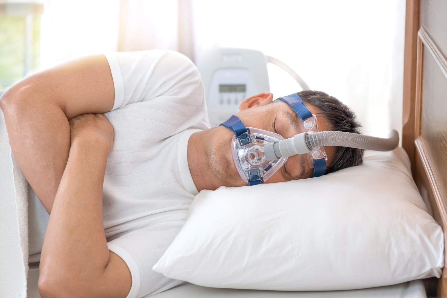 An elderly gentleman wears a breathing mask while lying on his side in bed trying to fall asleep.