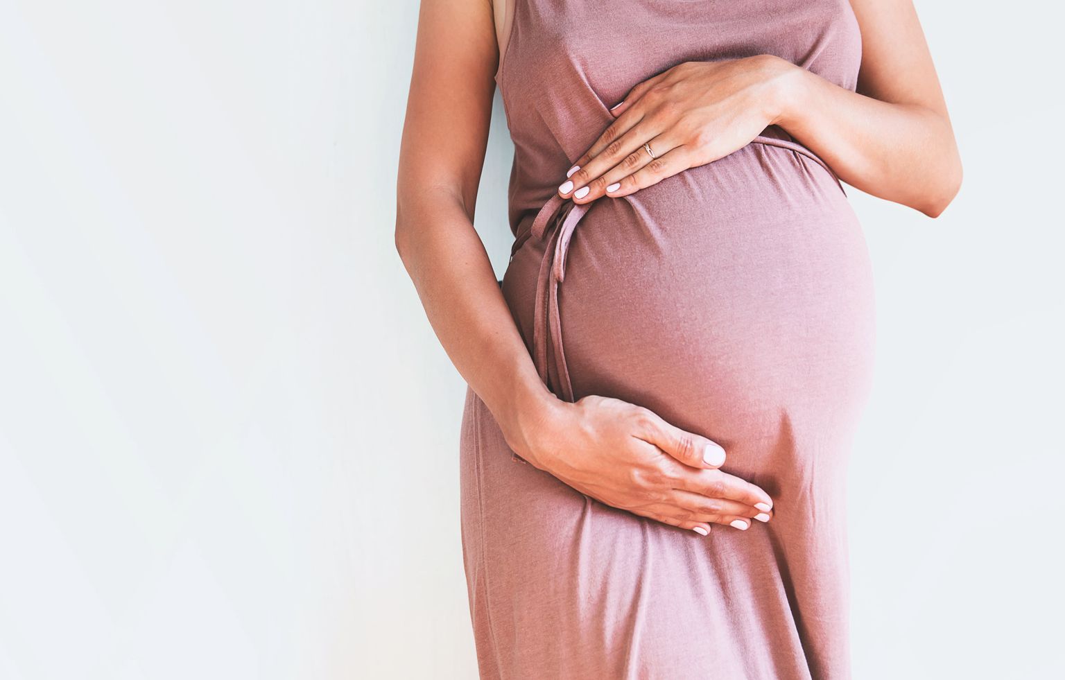 Eine schwangere Frau haltet ihren Bauch. Der Hintergrund ist weiß. 