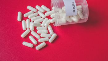 Pilules ou capsules placebo blanches s'écoulant d'une bouteille sur fond rouge, effet placebo, concept de randomisation ou de traitement, vue d'époque.